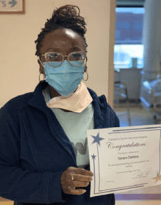 Tamara Clemons, a black female CCMH employee with retro glasses and a medical mask, holding her award
